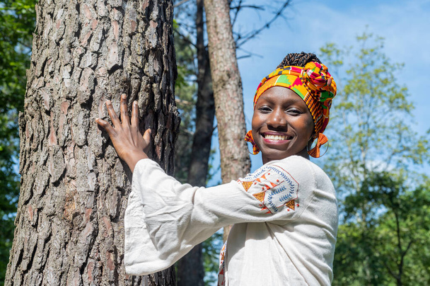 Νεαρή γυναίκα αγγίζει ένα δέντρο στο δάσος, ενώ χαμογελά - Φωτογραφία, εικόνα