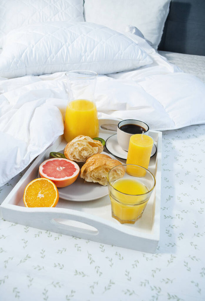 Πρωινό στο κρεβάτι. Καφές, κρουασάν, φρέσκος χυμός πορτοκαλιού και φρούτα. - Φωτογραφία, εικόνα