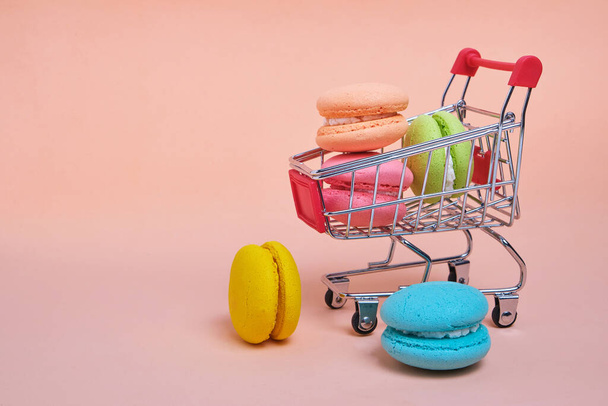 French macarons cookies in a shopping cart on a pink background - Zdjęcie, obraz