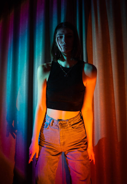 Young and sexy woman with wearing jeans and black t-shirt posing in colorful neon light - Foto, immagini