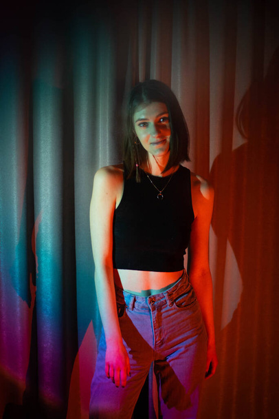 Young and sexy woman with wearing jeans and black t-shirt posing in colorful neon light - Fotoğraf, Görsel