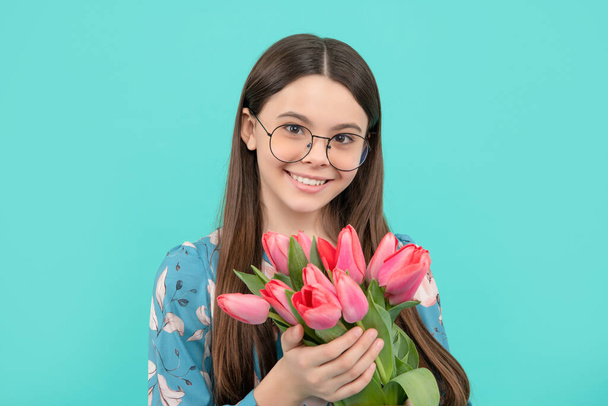 smiling child portrait in glasses with tulips. mothers or womens day. kid hold flowers for 8 of march. teen girl with spring bouquet on blue background. floral present. - Φωτογραφία, εικόνα
