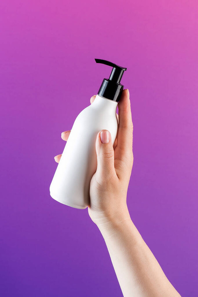 A mockup of a white dispenser with a cosmetic product in a womans hand on a purple background. Place for brand name. - Фото, зображення