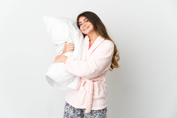 Young caucasian woman isolated on white background in pajamas and holding a pillow with happy expression - Foto, imagen