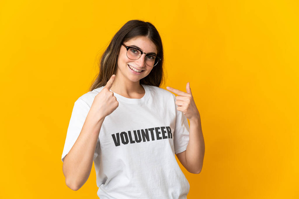 jonge vrijwilliger vrouw geïsoleerd op gele achtergrond het geven van een duim omhoog gebaar - Foto, afbeelding