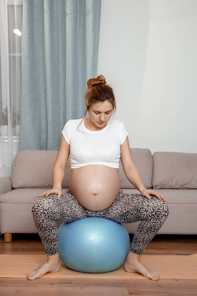 Pregnant woman exercising on fitball at home. Pregnant woman doing relax exercises with a fitness pilates ball. - Photo, Image