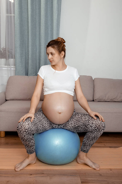 Terhes nő tornázik fitball otthon. Terhes nő csinál relaxációs gyakorlatok egy fitnesz pilates labda. - Fotó, kép