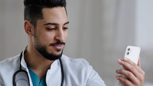 Zuversichtlich qualifizierter Arzt männlichen arabischen Arzt verwenden Smartphone Social Medical App konsultieren Kunden online in Klinik Kabinett Fernkommunikation geben Beratung telemedizinische Gesundheitsdienstleistungen Konzept - Foto, Bild