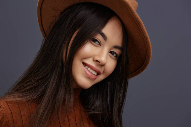 Brunette hattu hauskaa ruskea pusero poseeraa rento kulumista Harmaa tausta. Laadukas kuva - Valokuva, kuva
