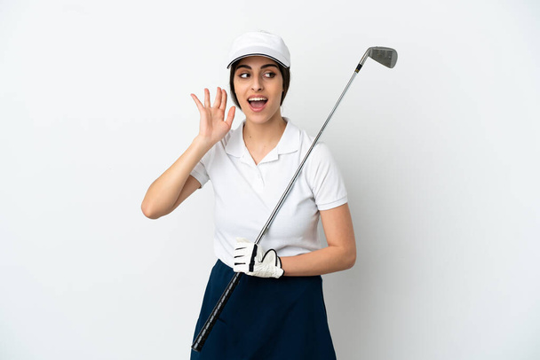 Guapo joven jugador de golf mujer aislado sobre fondo blanco escuchando algo poniendo la mano en la oreja - Foto, Imagen