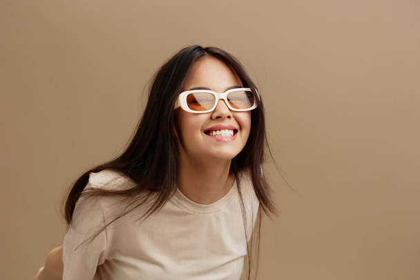 Gözlüklü, bej tişörtlü güzel bir kadın. Moda pozu veren, izole edilmiş bir arka plan. Yüksek kalite fotoğraf - Fotoğraf, Görsel