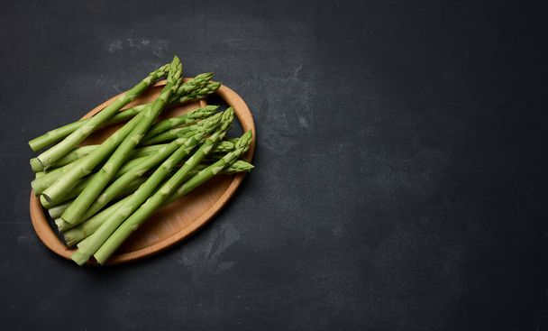 Bunch of fresh raw asparagus on a wooden black kitchen board, a healthy product - Фото, зображення