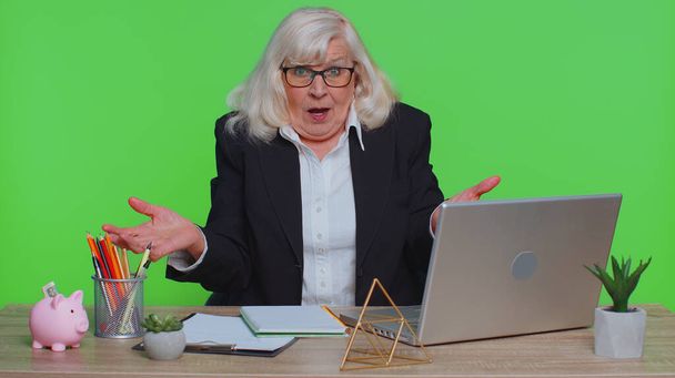 Ανώτερη επιχειρηματίας σηκώνει το χέρι στην αγανακτισμένη έκφραση ρωτώντας γιατί η αποτυχία δείχνει δυσπιστία από τα προβλήματα στο γραφείο. Ηλικιωμένη γυναίκα απομονωμένη στο πράσινο στούντιο chroma key - Φωτογραφία, εικόνα
