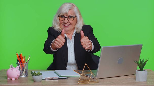 Starsza kobieta biznesu pracownik przy użyciu notebooka laptopa, podnosi kciuki w górę zgadza się z czymś lub daje pozytywną odpowiedź zaleca reklamy lubi dobre miejsca w biurze zielony chroma klucz - Zdjęcie, obraz