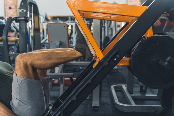 Close-up indoor shot of an unrecognizable caucasian man using a leg press. Man exercising in a modern gym. Healthy lifestyle concept. High quality photo - Photo, Image