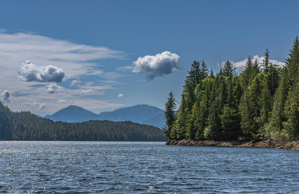 Ketchikan, Alaska, USA - July 17, 2011: Blue cloudscape above landscape of green forests on island shorelines behind blue ocean water. Tall mountains on horizon. - Foto, Imagen