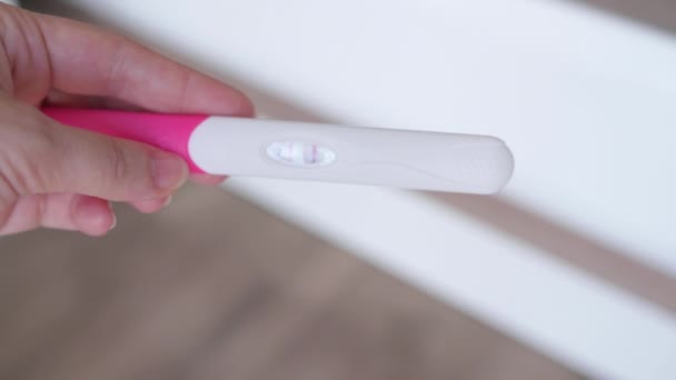 妊娠検査を夫に示す妻。2本の線で男の陽性妊娠検査に与える女性の手のショットを閉じます.妊娠の概念、家族計画. - 映像、動画