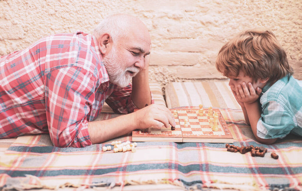 Kid Playing Chess. Grandfather and grandson are playing chess and smiling while spending time together at home. Chess competition - Фото, изображение