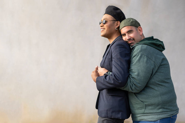 Schwules lateinisches Paar mit modischen Hüten, das sich auf der Straße umarmt. Kopierraum - Foto, Bild
