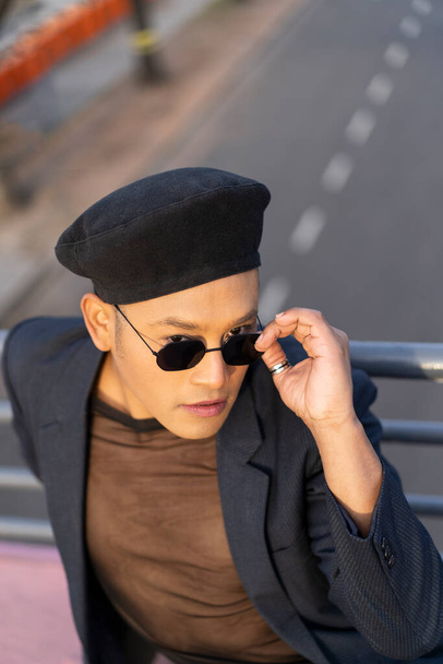 Makyajlı, modaya uygun şapkalı, köprüde poz veren Latin eşcinsel erkek. - Fotoğraf, Görsel