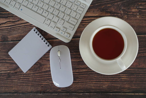 bloc de notas y una taza de té con equipos informáticos sobre la mesa - Foto, Imagen