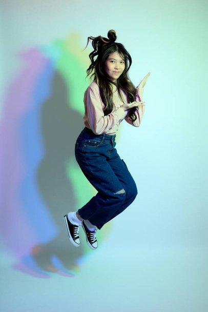 Cute młoda Azjatka dziewczyna z casual ubrania pozowanie pod kolor żelu piorun w studio. - Zdjęcie, obraz
