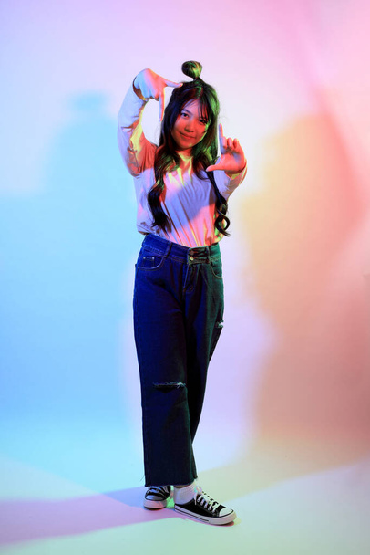 De schattige jonge Aziatische meisje met casual kleding poseren onder de gel kleur bliksem in de studio. - Foto, afbeelding