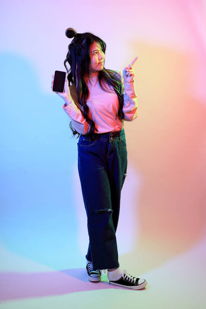 Το χαριτωμένο νεαρό κορίτσι της Ασίας με casual ρούχα που ποζάρουν κάτω από το χρώμα τζελ αστραπή στο στούντιο. - Φωτογραφία, εικόνα