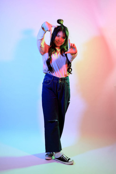 La jeune fille asiatique mignonne avec des vêtements décontractés posant sous la foudre de couleur de gel en studio. - Photo, image