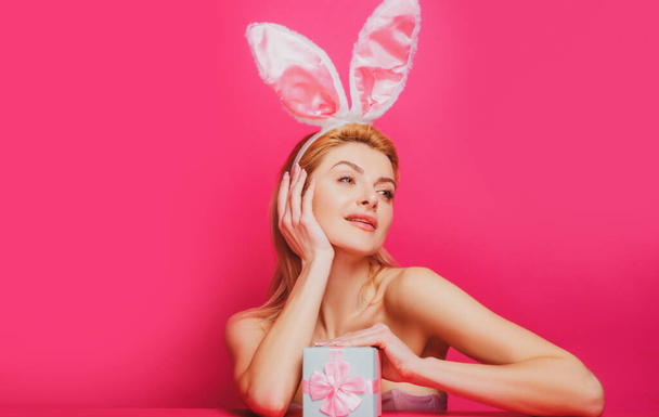 Beautiful young sexy bunny woman with prasent gift isolated on pink - 写真・画像