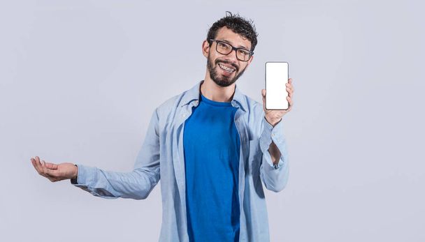 Handsome man smiling positive showing mobile phone blank screen with another hand palm open, excited happy male holding smartphone  - Фото, изображение