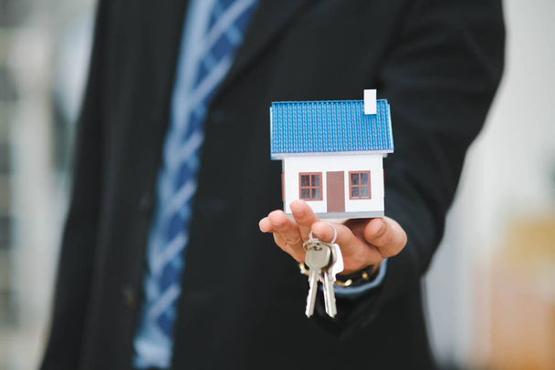 Üzletember kezében egy ház modell és a ház kulcsai. - Fotó, kép