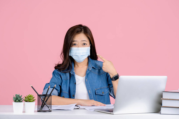 Joven mujer de negocios asiática en ropa casual y con una máscara para prevenir covid 19 aislado en el estudio de fondo rosa. - Foto, imagen