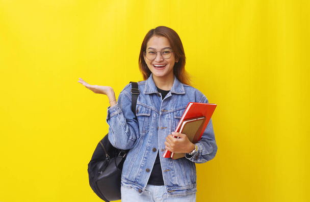 Happy asian young woman standing while presenting something. Isolated on yellow background - Foto, immagini