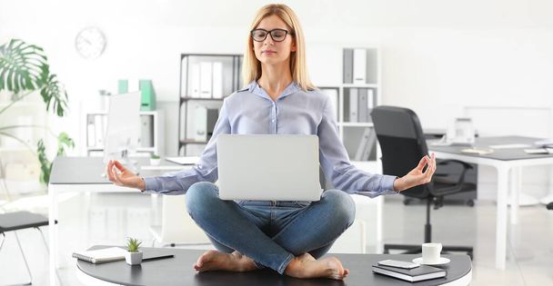 Beautiful businesswoman with laptop meditating in office - Photo, Image