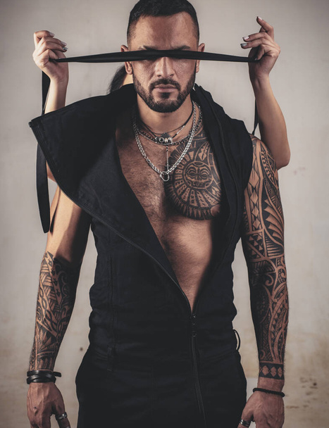 trust concept. muscular macho man with athletic body. brutal sportsman. steroids. dominating. sexy abs of tattoo man. male fashion. female hands cover his eyes with rope. censorship. Human Right day. - Foto, Bild