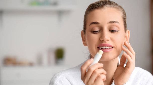 Beautiful young woman applying lip balm in bathroom - Photo, Image