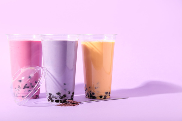 Tazas de plástico de té de burbujas diferentes sabroso sobre fondo púrpura - Foto, Imagen