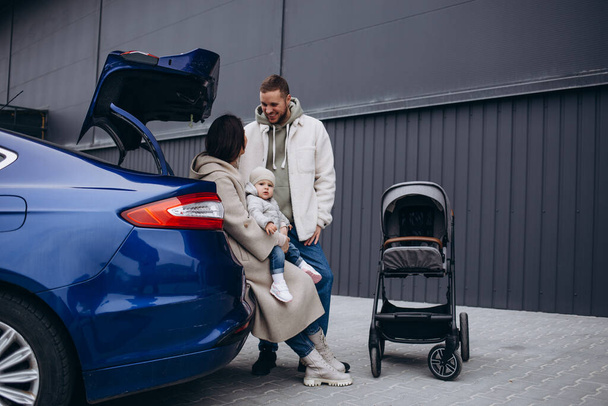 Mutter und Tochter laden die Batterie eines Elektroautos. Im Hintergrund holt Papa den Kinderwagen aus dem Kofferraum - Foto, Bild