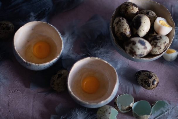 quail eggs in ceramic vases, gray feathers on the table, easter still life, natural food, diet and antioxidants, dark key and shallow depth of field. High quality photo - Fotografie, Obrázek