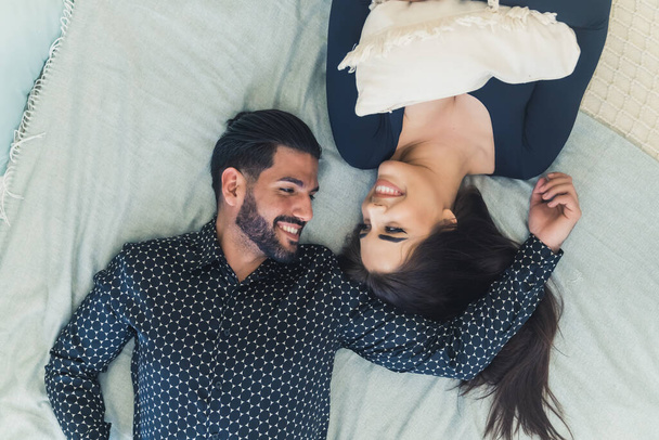 Love between two people. Happy heterosexual married couple lying on bed, looking each other in the eye in a romantic way, and smiling. High quality photo - Valokuva, kuva