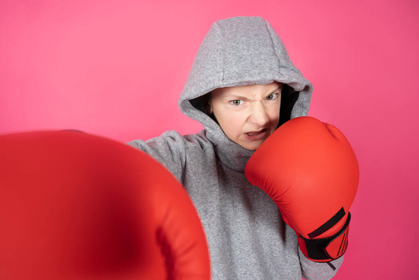 Violent boy wearing hoodie giving a punch using boxing gloves isolated on vivid pink background. Violence at childhood and bullying concept - Foto, Imagem