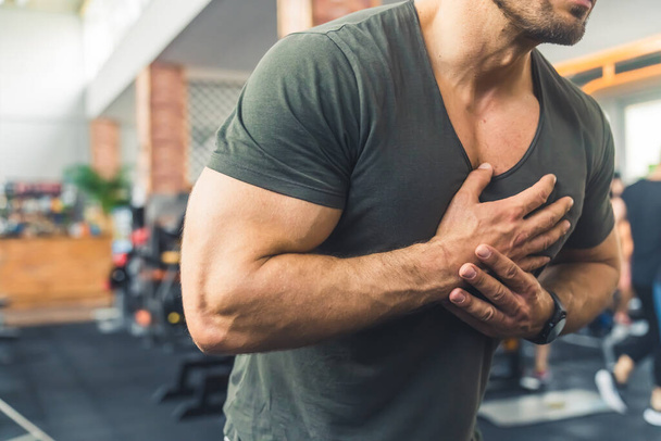 Kopflose Schüsse in einem Fitnessstudio auf einen bärtigen Mann mittleren Alters in einem lässigen T-Shirt, der seine Hände auf der Brust hält und einen Herzinfarkt erleidet. Hochwertiges Foto - Foto, Bild