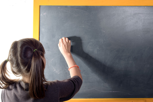 a little girl with pigtails writes on a blackboard - Foto, afbeelding