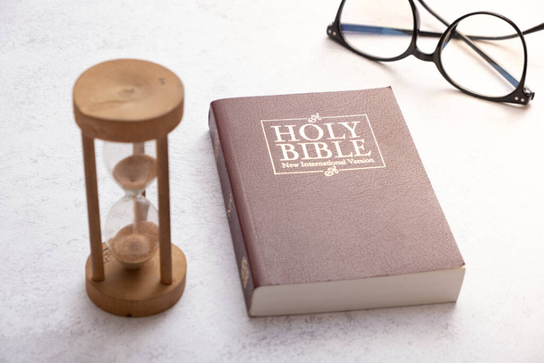 Верхний вид Библии на рабочем столе с песочными часами. Концепция времени изучения Библии. - Фото, изображение