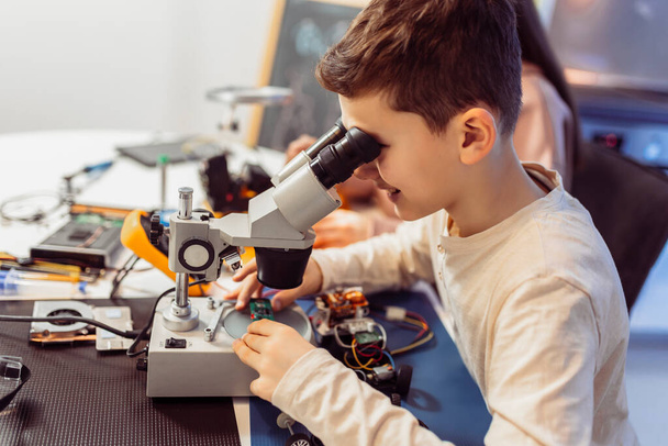 Τα παιδιά φτιάχνουν ρομπότ στο σπίτι χρησιμοποιώντας μικροσκόπιο. Εκπαίδευση στη ρομποτική στο σπίτι. - Φωτογραφία, εικόνα
