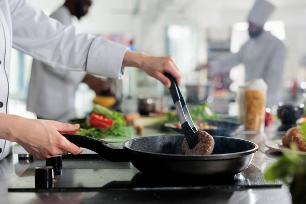 Meisterkoch reicht Rindfleisch-Patty in heißer Pfanne, während er Gourmet-Gericht für den Abendessen zubereitet. Facharbeiter in der Lebensmittelindustrie braten Hackfleisch in der professionellen Küche des Restaurants. - Foto, Bild