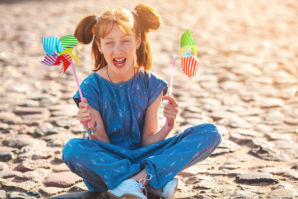 Leuk grappig klein meisje met windmolen. Een kind met een windmolen. Achtergrond van de zomertijd. - Foto, afbeelding