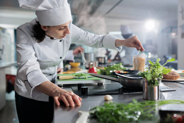 Culinary expert putting fresh chopped herbs in pan while cooking gourmet dish for dinner service at fine dining restaurant. Head chef preparing organic meal in professional kitchen. - Photo, Image