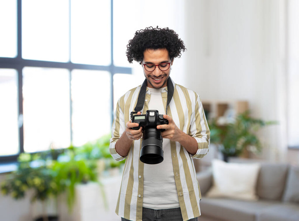 photography, profession and people and concept - happy smiling man or photographer in glasses with digital camera over home room background - Fotografie, Obrázek